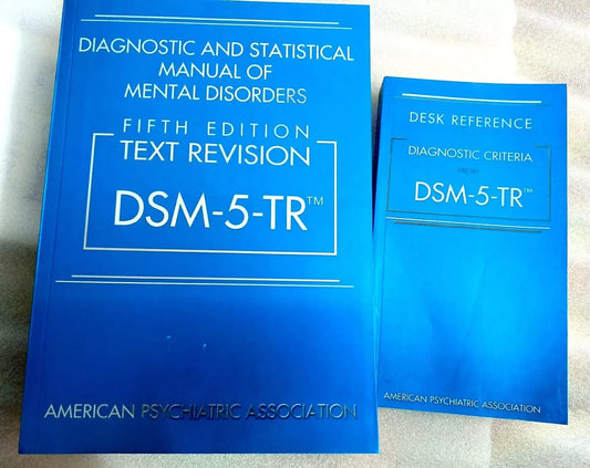 Two bright blue books titled Diagnostic and Statistical Manual of Mental Disorders DSM-5-TR sit side by side on a flat surface, with the larger edition on the left and a smaller desk reference on the right.